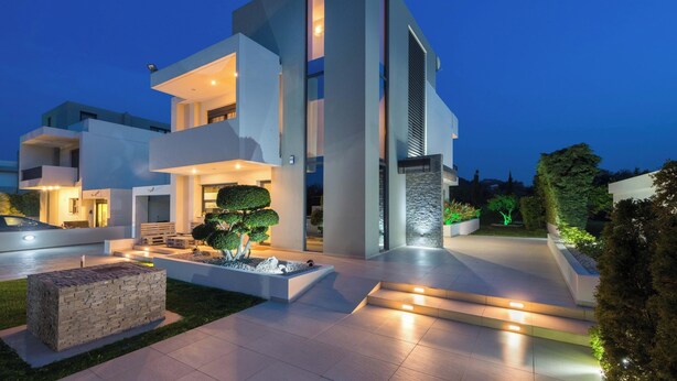 Una casa moderna de varios pisos con un camino bien iluminado y un jardín ajardinado.