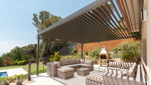A covered outdoor seating area with wicker furniture, a pergola, and a view of a landscaped garden. -  Spacious family villa with pool, sea view, sauna, 10-14 persons (Sant Andreu de Llavaneres)
