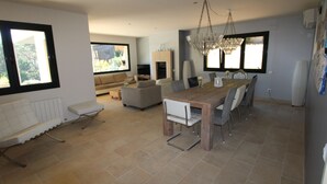 A spacious living area with a dining table, sofas, and a fireplace. -  Spacious family villa with pool, sea view, sauna, 10-14 persons (Sant Andreu de Llavaneres)