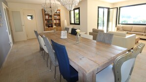 A spacious dining area with a wooden table and chairs, a chandelier, and a bookshelf. -  Spacious family villa with pool, sea view, sauna, 10-14 persons (Sant Andreu de Llavaneres)