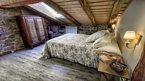 A rustic bedroom with a stone wall, wooden beams, a bed with a floral bedspread, a wooden wardrobe, and a nightstand with a lamp. - The Rural Apartment - Maria's Rural House (Terán, Cabuerniga)