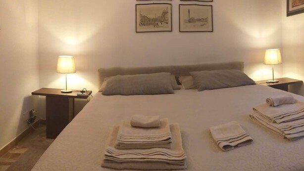 A neatly made bed with folded towels, two bedside tables with lamps, and four framed pictures on the wall. - bed room yacopino. (Firenze)
