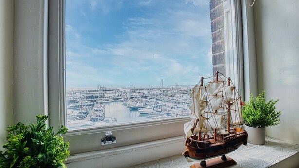 A model ship on a windowsill with a view of a marina.