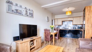 A modern living room with a TV, wooden entertainment unit, and a dining area with a table and chairs.