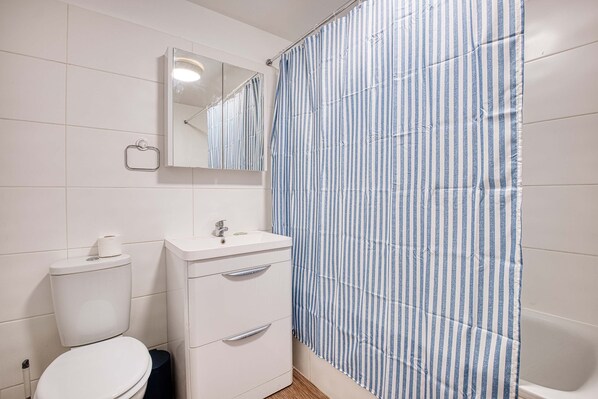 A bathroom with a toilet, sink, mirror, and a shower curtain. - Harbour View | Central | Iconic View | Coastal Stay (Ramsgate)