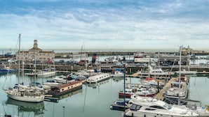 A marina with boats docked, a building with a clock tower, and a clear sky.
