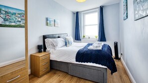 A bedroom with a bed, bedside table, dresser, and a window with curtains.