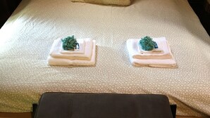 Een net opgemaakt bed met een bedsprei met een patroon, twee gevouwen handdoeken met groene accenten, en een nachtkastje met een lamp.