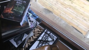 Een houten terras met een touwen schommel, een boek met de titel 'Living in Bali' en een houten klomp op de vloer.