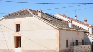 A two-story building with a sloped roof, a small window on the ground floor, and a stone wall on the right side. - Casa de la Maestra for 10 people (Barbolla)