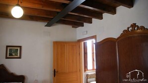 A room with exposed wooden beams, a wooden wardrobe, a bed with a headboard, and a framed picture on the wall. - Casa de la Maestra for 10 people (Barbolla)
