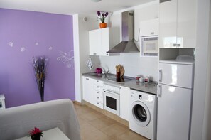 Cozinha compacta com armários brancos, micro-ondas embutido, coifa de aço inoxidável e máquina de lavar com abertura frontal.