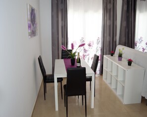 Uma área de refeições com uma mesa branca, cadeiras pretas e um aparador branco.