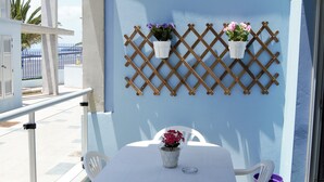A balcony with a white table, two chairs, and two potted plants on a blue wall. - Cozy apartment in Muelle Deportivo Morro Jable, pets are allowed. (Morro Jable)