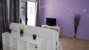 A living room with a white sofa, a TV on a white stand, and a purple wall with floral decals. - Cozy apartment in Muelle Deportivo Morro Jable, pets are allowed. (Morro Jable)