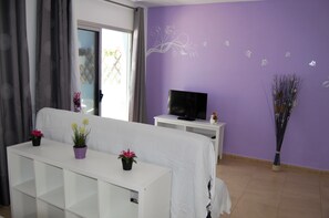 Uma sala de estar com um sofá branco, uma TV sobre um suporte branco e uma parede roxa com adesivos florais.