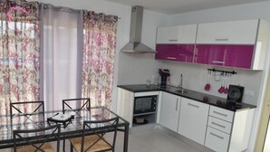 A modern kitchen with white and purple cabinets, a stainless steel range hood, and a glass dining table with chairs. - Escondidinho Houses - Casa da Eira (Bajouca, Leiria)