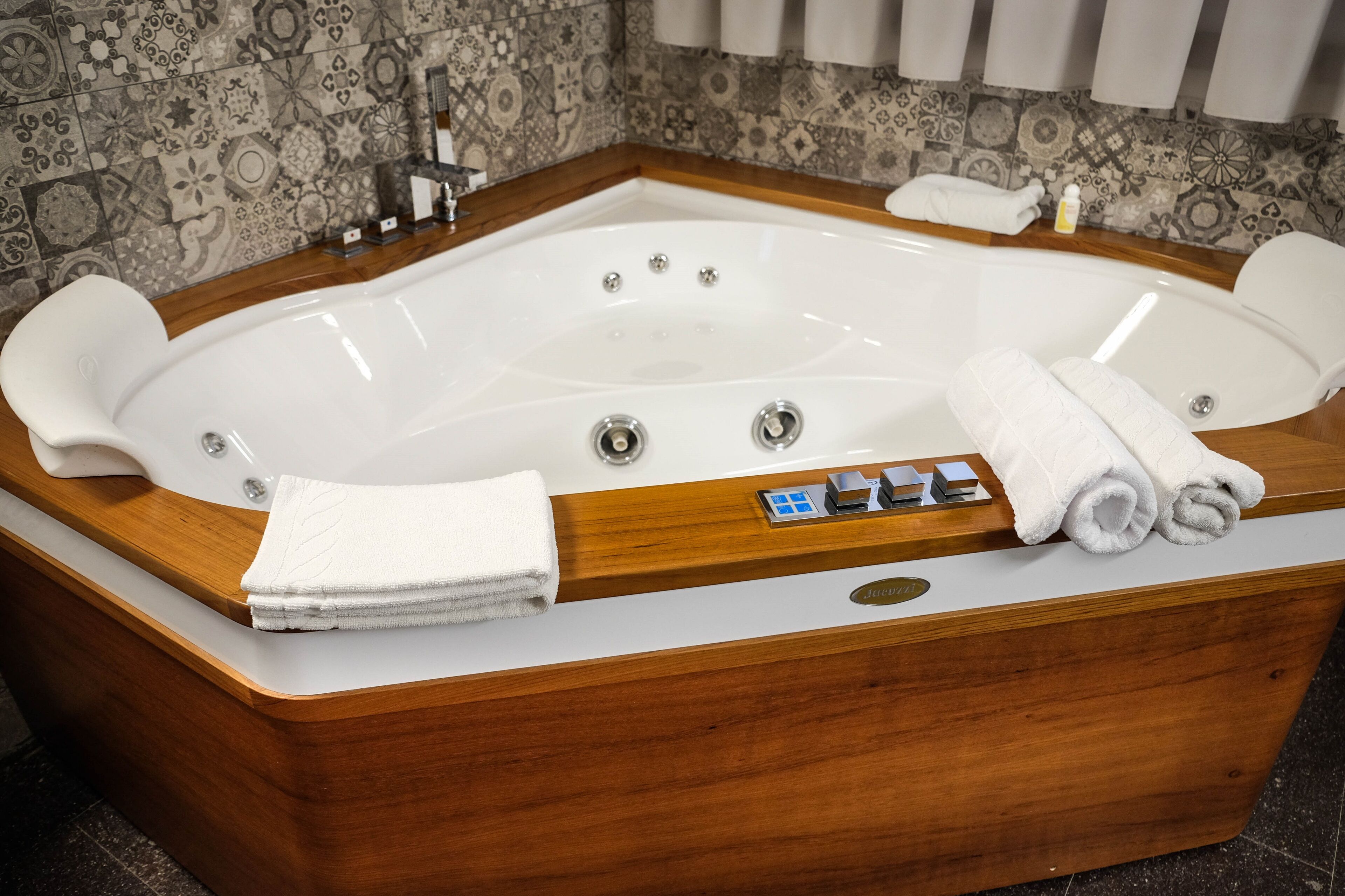 A large, rectangular hot tub with a wooden frame and control panel, surrounded by a tiled wall and a wooden countertop.