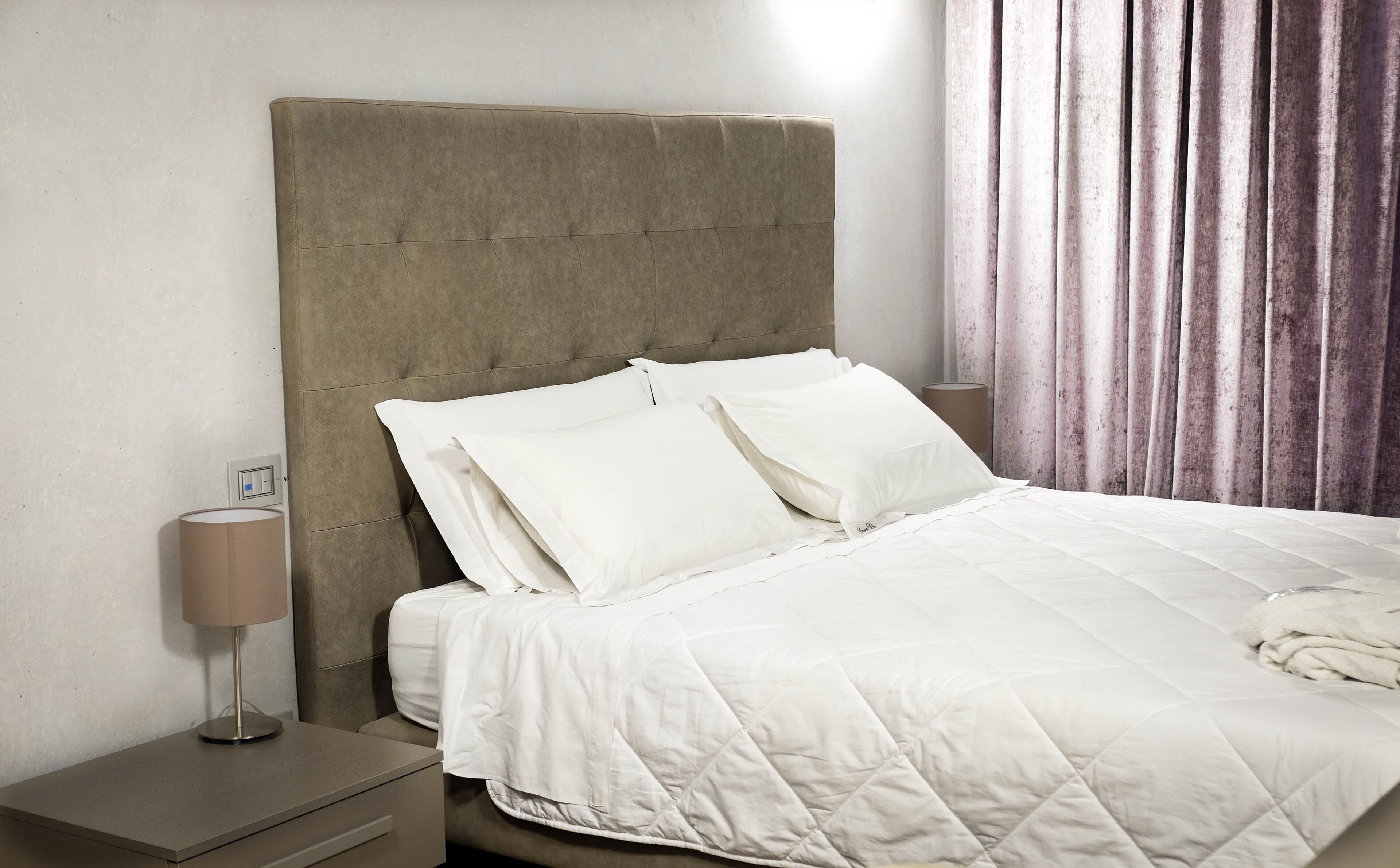 A neatly made bed with white bedding, a headboard, and two bedside tables with lamps.