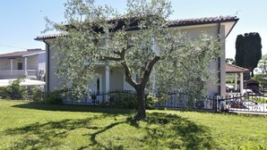 Ein Haus mit Baum davor, einem eingezäunten Garten und blauem Himmel.