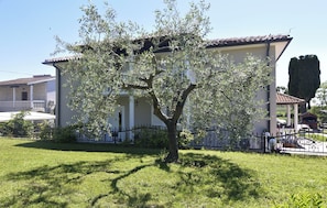 Una casa con un árbol en el frente, patio cercado y cielo despejado.