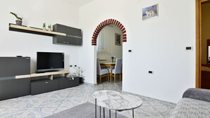 Ein modernes Wohnzimmer mit Flachbildfernseher, integrierten Regalen, einem Essbereich mit Tisch und Stühlen sowie einem Musterparkett.
