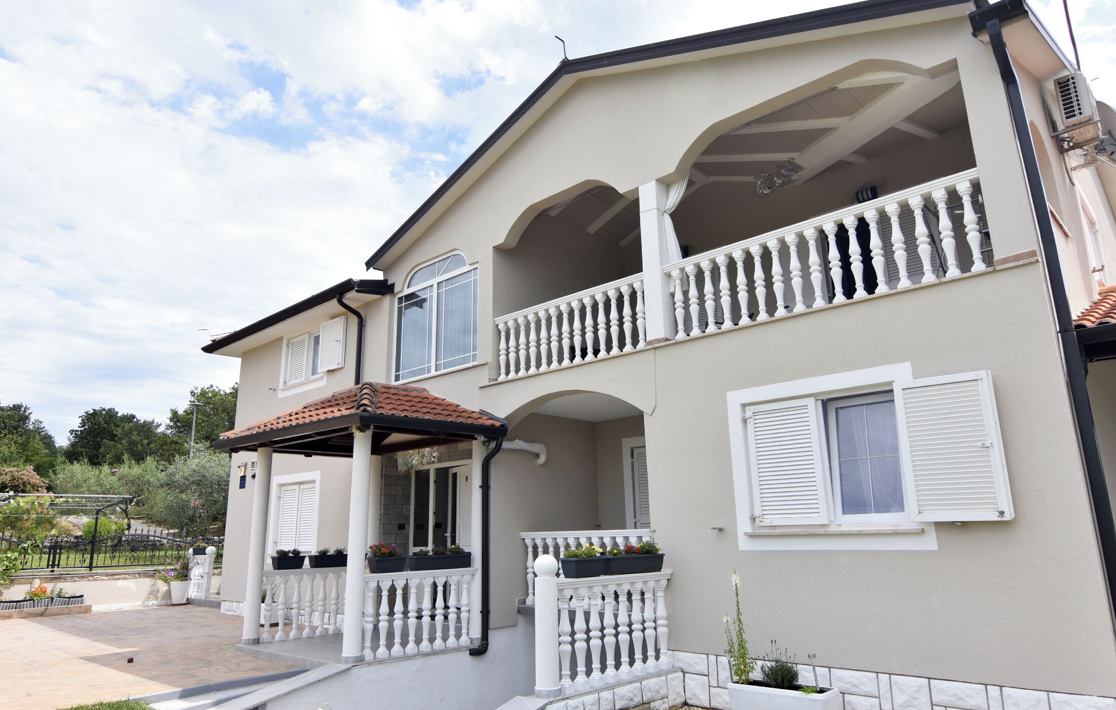 A two-story building with balconies, a covered porch, and a garden area.