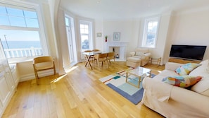 A spacious living room with a wooden floor, a white sofa, a TV, and a fireplace.