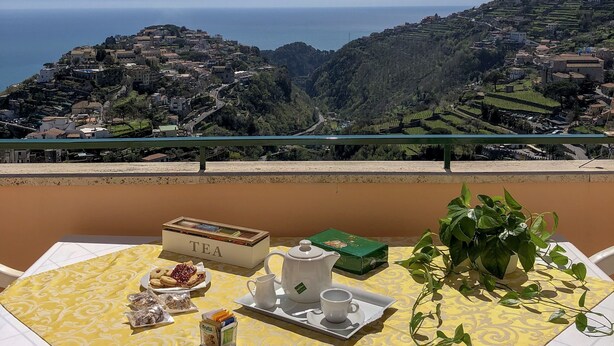 A balcony table with a yellow tablecloth, a teapot, cups, and a box labeled "TEA". - House Joseph with beautiful view and private parking (Ravello)