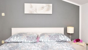 A bedroom with a bed, a bedside lamp, a wall-mounted light fixture, and a floral artwork on the wall.