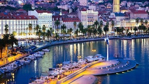 A marina with boats docked, a waterfront promenade, and historic buildings in the background.