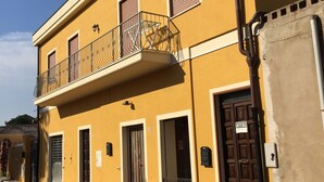 A yellow building with a balcony, a door with a sign, and a cobblestone street.