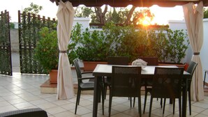 Un patio al aire libre con una mesa y sillas, rodeado de plantas en macetas y una pérgola.