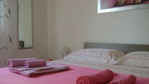 Una cama bien hecha con ropa de cama rosa y toallas enrolladas a un lado.