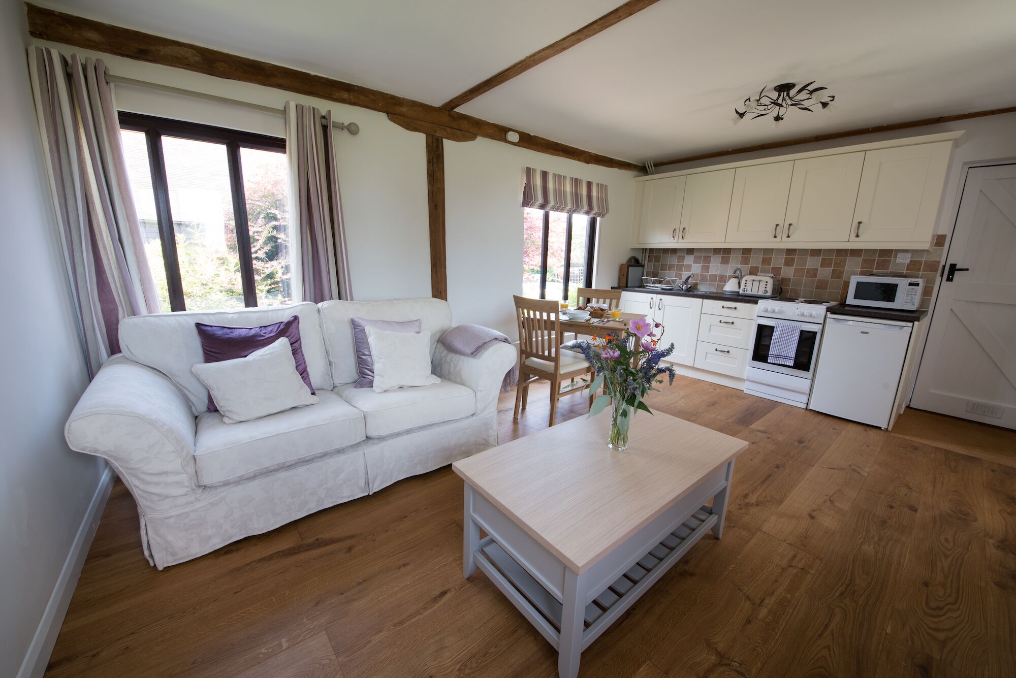 A cozy living room with a sofa, a coffee table, and a dining area with a table and chairs. A kitchen with cabinets and appliances is visible in the background.