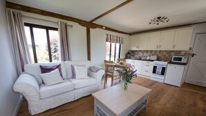 A cozy living room with a sofa, a coffee table, and a dining area with a table and chairs. There is a kitchen with cabinets, a stove, and a microwave. - Tastefully Renovated Countryside Cottage with Swimming Pool near Tenterden (High Halden)