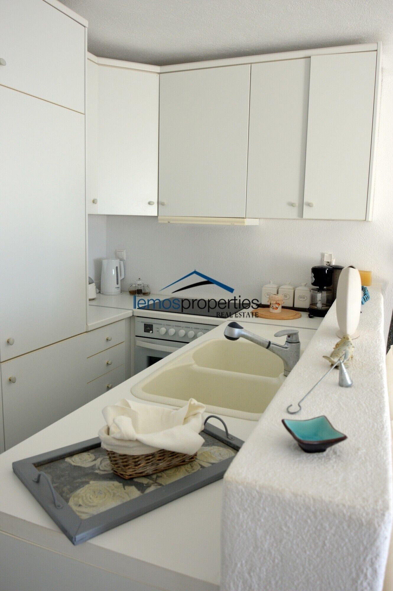 Una cucina con mobili bianchi, un fornello, un lavello e un piano di lavoro con un cesto e un piccolo piatto.