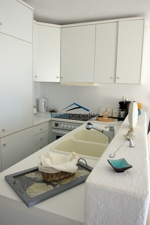 A kitchen with white cabinets, a stove, a sink, and a countertop with a basket and a small dish.