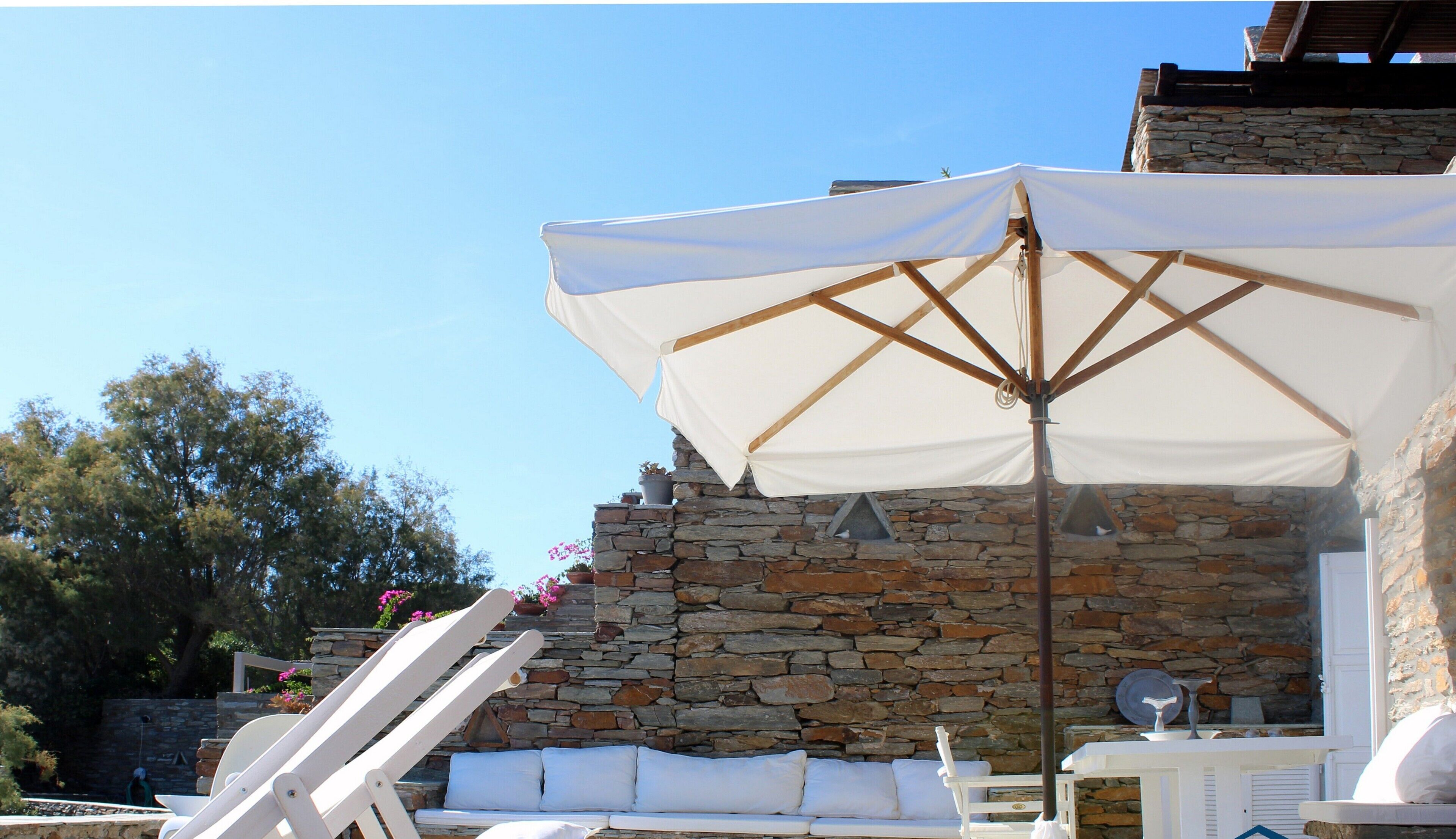 A stone wall with a white umbrella and lounge chairs.