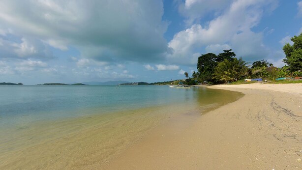 A beach with clear water, a sandy shore, and a few boats.