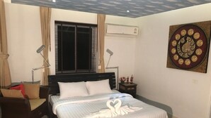 A bedroom with a bed, bedside lamps, a nightstand, a window with blinds, an air conditioning unit, and a wall decoration.