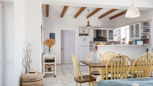 A compact kitchen with white cabinets, a wooden dining table, and yellow chairs. - Villa Paros - Archipelagos Villas with Pool close to the sea (Naousa Paros)