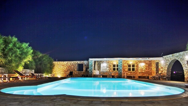 A stone building with a swimming pool, outdoor seating, and a night sky. - Villa Paros - Archipelagos Villas with Pool close to the sea (Naousa Paros)