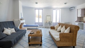 A living room with a dark sofa, a wicker sofa, a small table with a hat, and a desk with a chair. - Villa Paros - Archipelagos Villas with Pool close to the sea (Naousa Paros)