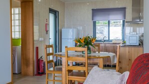 Un salon avec un canapé rouge à motifs, une table à manger en bois avec des chaises, un coin cuisine avec un réfrigérateur et une fenêtre donnant sur un paysage agréable.