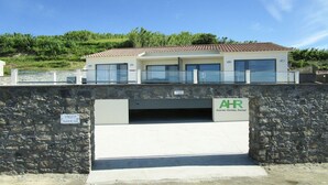 Un bâtiment moderne avec un toit en tuiles, de grandes fenêtres et une entrée surmontée d’un mur en pierre.