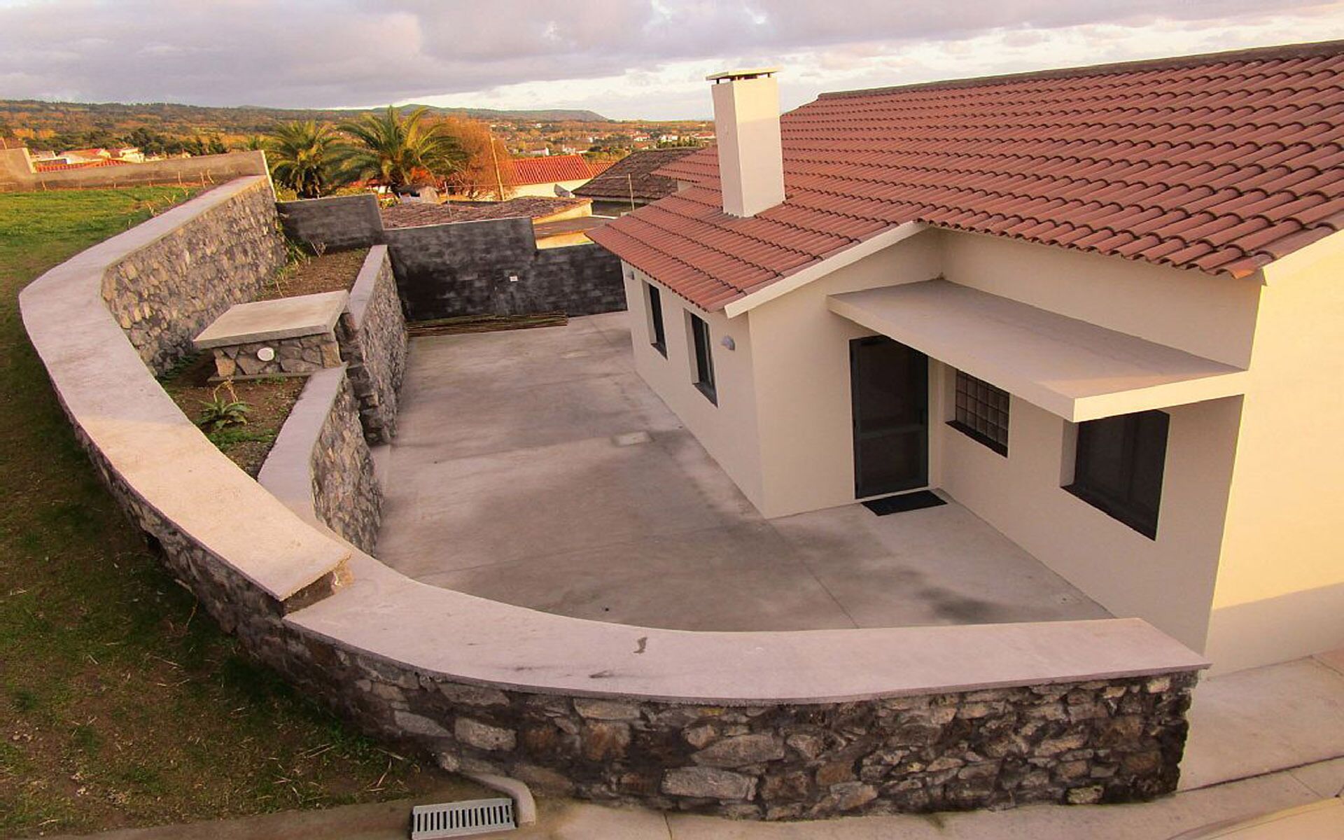 Ein modernes Haus mit einer gewölbten Steinwand, einem roten Ziegeldach und einer Beton-Terrasse.