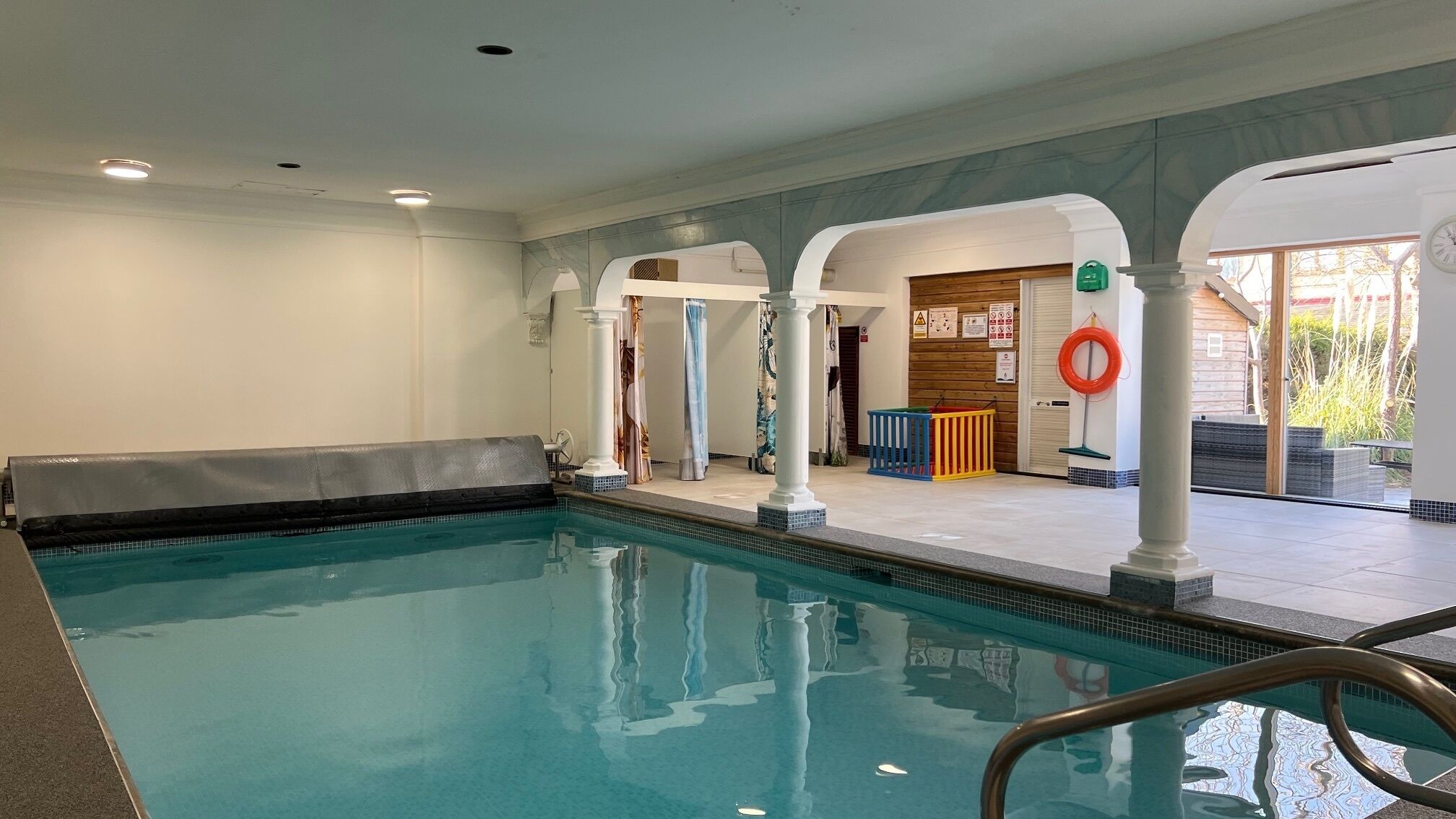 Ein Innenpool mit klarem Wasser, umgeben von weißen Säulen und einem gefliesten Boden.