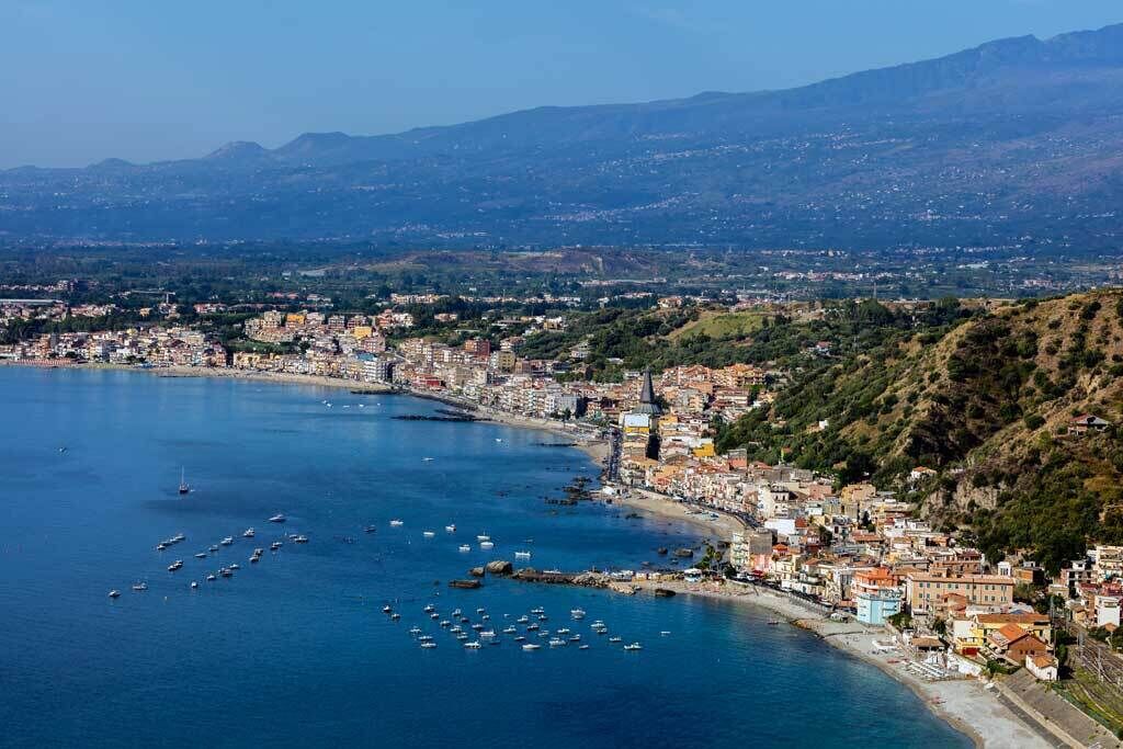 A coastal cityscape with a densely packed urban area, a large body of water with numerous boats, and a mountainous backdrop.