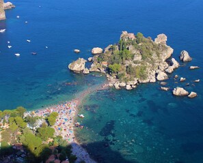 Luchtbeeld van een kustgebied met een strand, rotsformaties en boten.